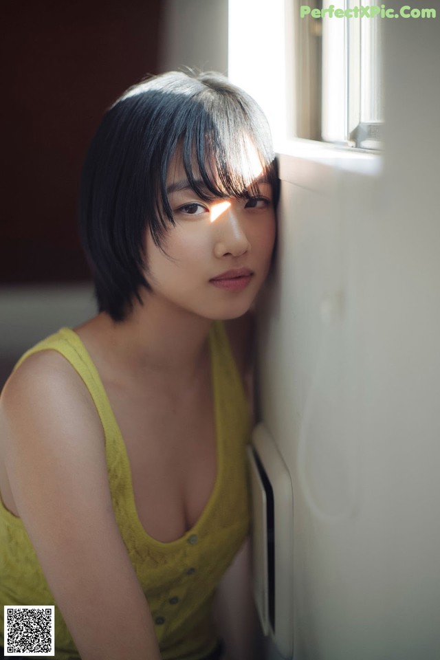 A woman leaning against a wall next to a window.