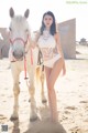 A woman in a white lingerie standing next to a white horse.