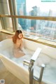 A naked woman sitting in a bathtub in front of a window.