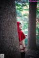 A woman in a red hooded outfit standing next to a tree.