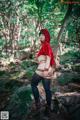 A woman in a red hoodie is posing in the woods.