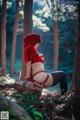 A woman in a red hooded outfit sitting in the woods.