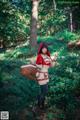 A woman dressed as a red riding hood holding a basket in the woods.