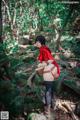 A woman in a red riding hoodie standing on a rock in the woods.