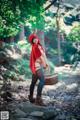 A woman in a red hooded outfit holding a basket in the woods.