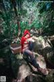 A woman in a red hoodie sitting on a rock in the woods.