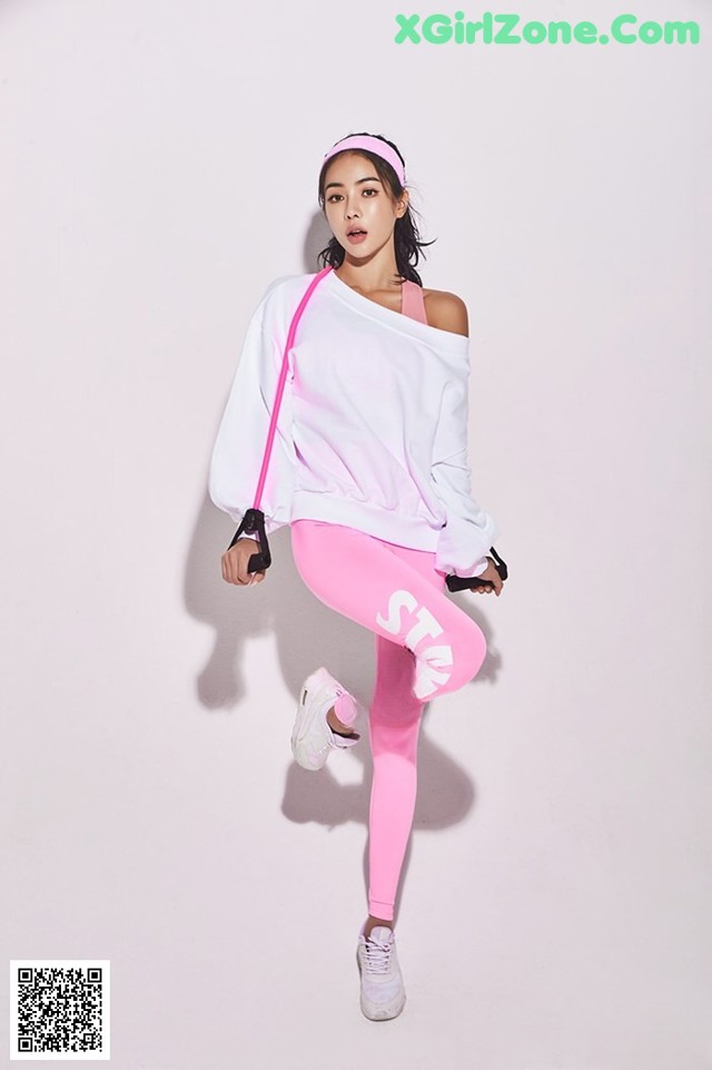 A woman in a white sweatshirt and pink leggings posing for a picture.