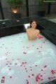 A woman sitting in a bathtub filled with rose petals.