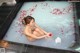 A woman sitting in a bathtub filled with water and rose petals.