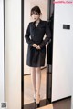 a woman in a black trench coat standing in front of a mirror