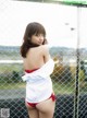 A woman in a white shirt and red panties posing by a fence.