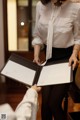 A woman in a white shirt and black skirt holding a folder.