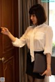 A woman in a white shirt and black skirt opening a door.