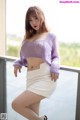 A woman in a purple sweater and white skirt posing for a picture.