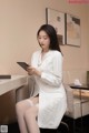 A woman in a white lab coat sitting on a chair looking at a tablet.