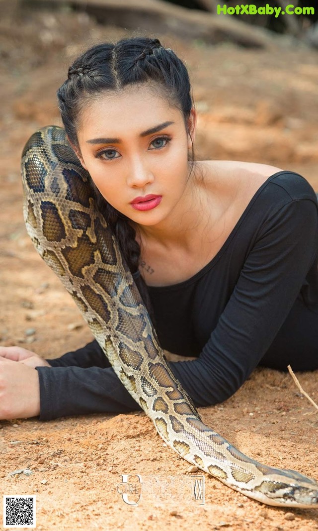 A woman laying on the ground with a snake around her neck.