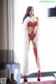 A woman in a red lingerie and red stockings posing by a window.