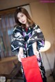 A woman in a black and purple kimono holding a red bag.