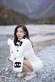 A woman in a white sweater and scarf sitting on a beach.