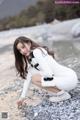 A woman in a white dress crouching on a rocky beach.