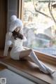 A woman sitting on a window sill wearing a white dress and hat.