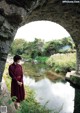 A woman in a red dress standing in front of a stone archway.