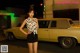 A woman standing in front of a yellow car at night.