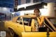 A woman leaning on the door of a yellow car.