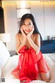 A woman in a red dress sitting on a bed.