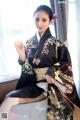 A woman in a black kimono sitting on a bed holding chopsticks.