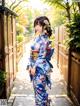 A woman in a blue kimono standing in front of a fence.