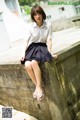 A woman in a white shirt and black skirt sitting on a stone wall.