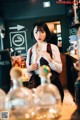 A woman standing behind a bar with bottles of alcohol.