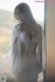 A woman in a white lingerie standing by a window.