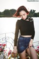 A woman in a black top and denim skirt posing by the water.